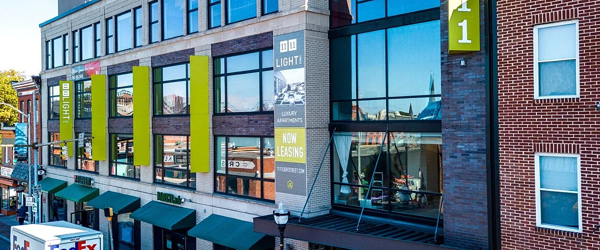Modern urban building with large glass windows, showcasing luxury apartments for lease in a bustling city street setting.