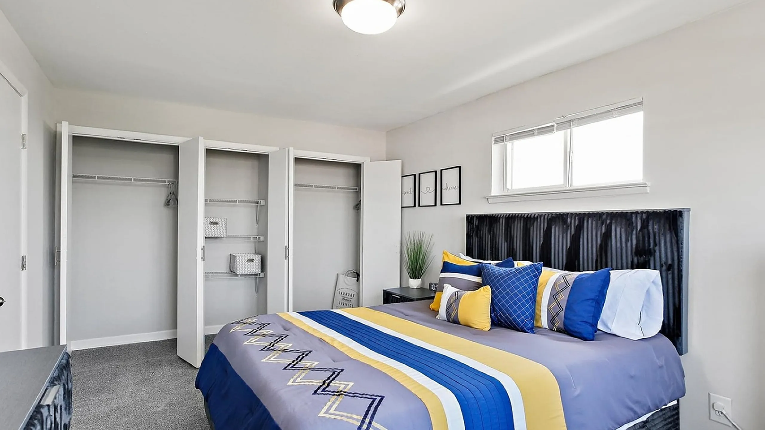 Modern bedroom with vibrant bedding, open closets, and natural light streaming through a window, creating a bright and inviting atmosphere.