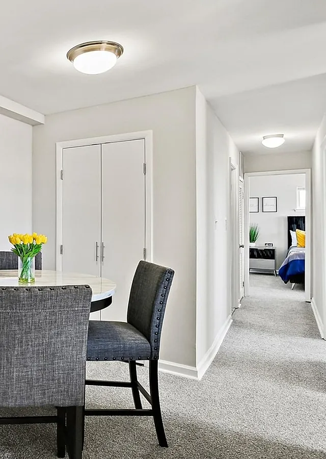 Contemporary apartment dining area with a round white table, elegant gray chairs, and decorative potted plant, leading to a cozy bedroom.
