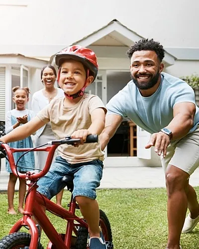 Vibrant family enjoying outdoor fun, with a child learning to ride a bike in a beautiful garden setting.