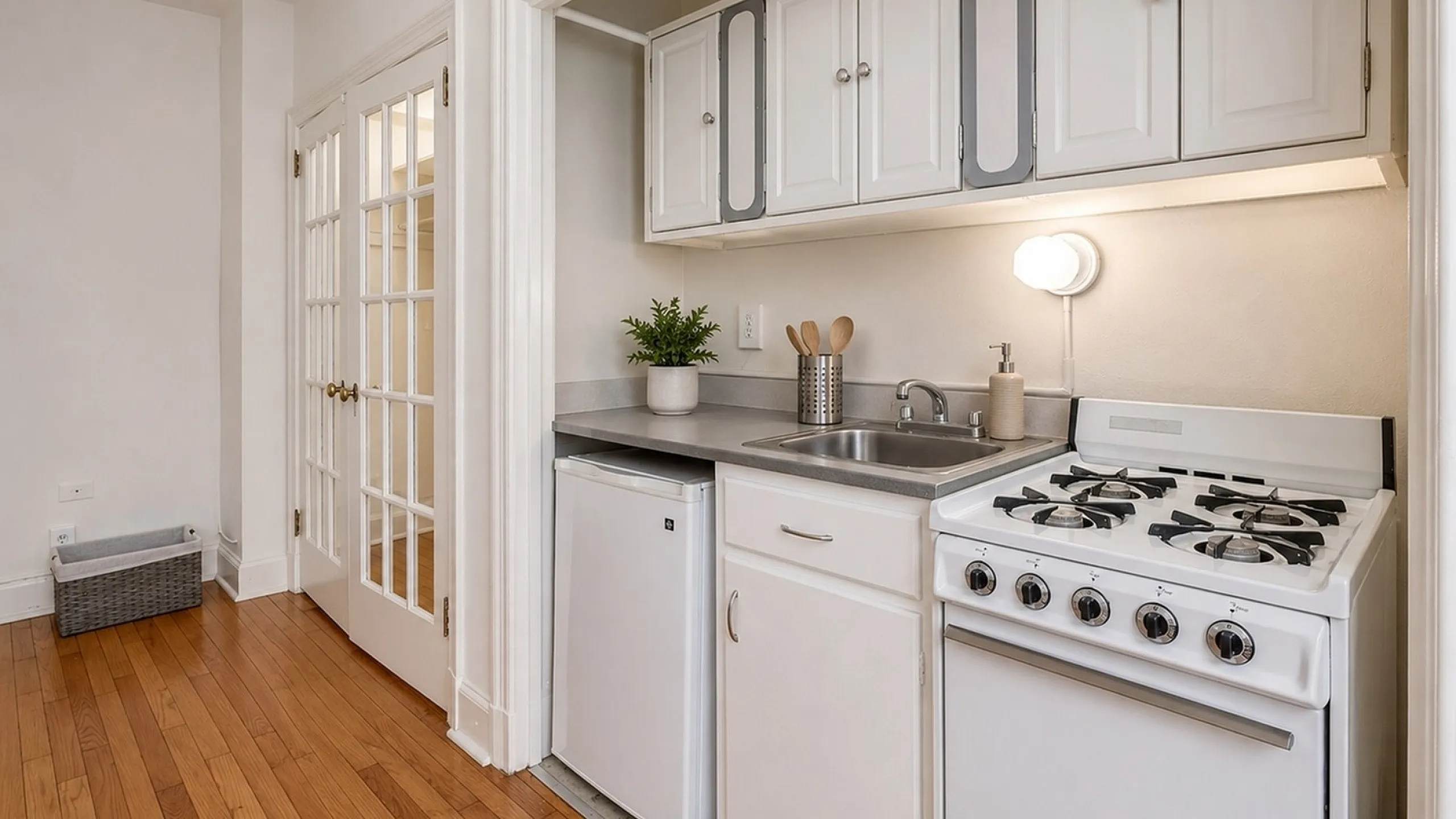 Charming compact kitchen with sleek white cabinetry, modern appliances, and elegant hardwood flooring.