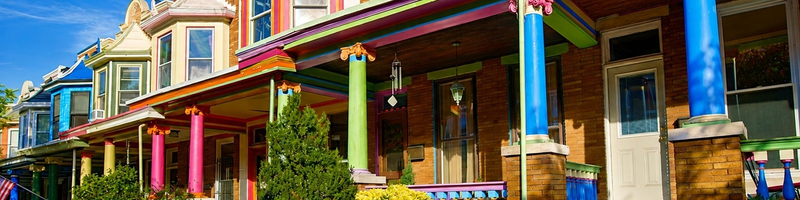 Vibrant row houses with colorful facades and ornate columns, showcasing playful architecture and lush greenery.