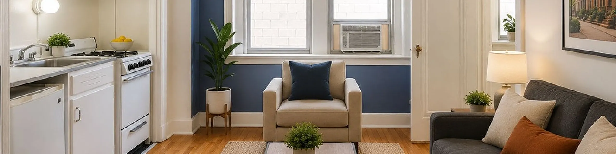 Cozy living room featuring elegant blue accent wall, comfortable seating, and compact kitchen nook with chic cabinetry.
