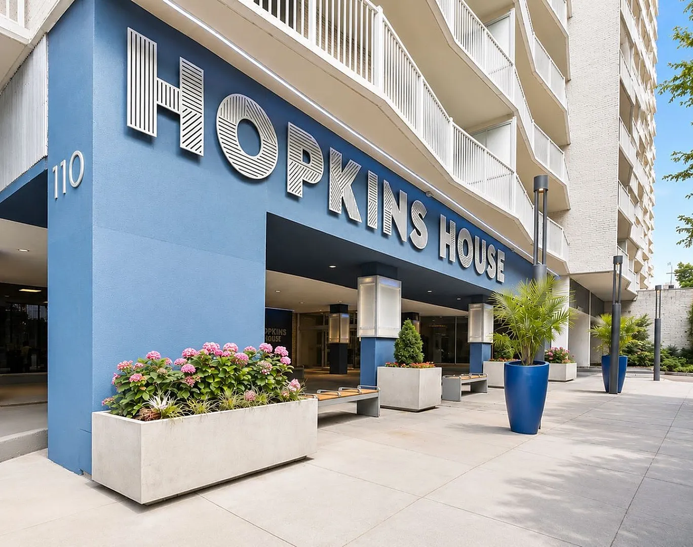Modern apartment building exterior featuring 'Hopkins House' with inviting entrance, stylish planters, and blue facade.