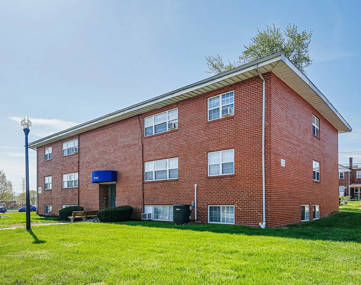 Charming red brick apartment building with well-maintained lawn and clear blue skies, offering a cozy and inviting residential experience.