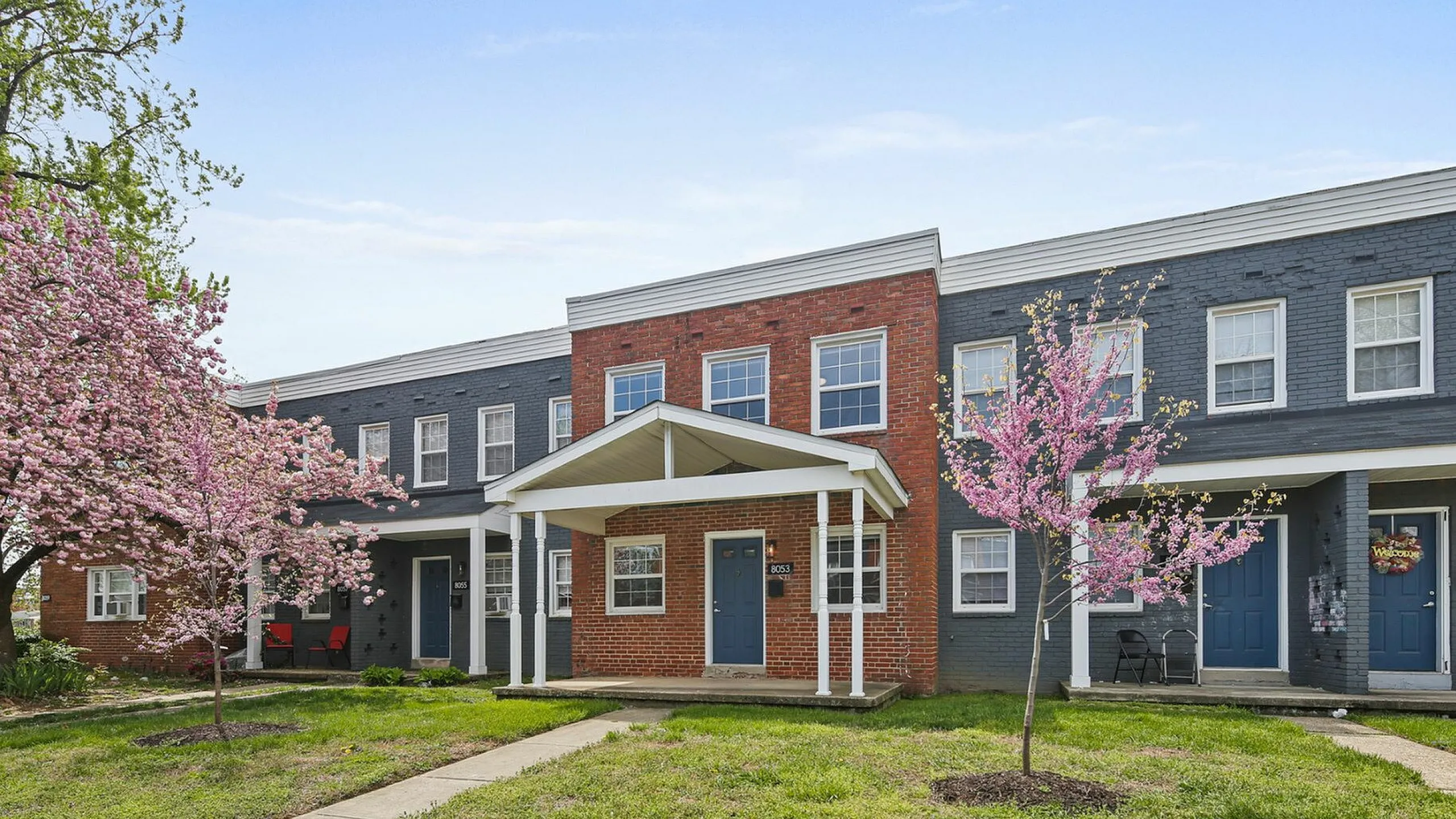 Charming brick apartment facade with blooming cherry blossom trees, offering a serene and inviting residential ambiance.