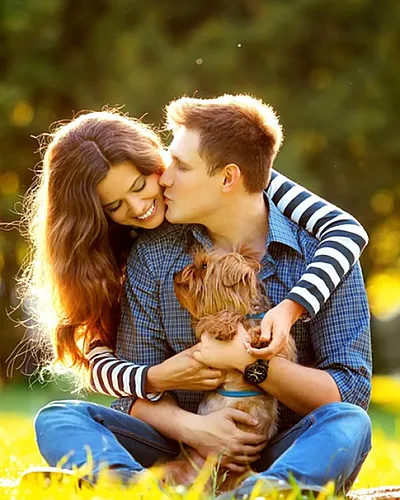 Happy couple enjoying a sunny day in the park, sitting on the grass with their adorable small dog.