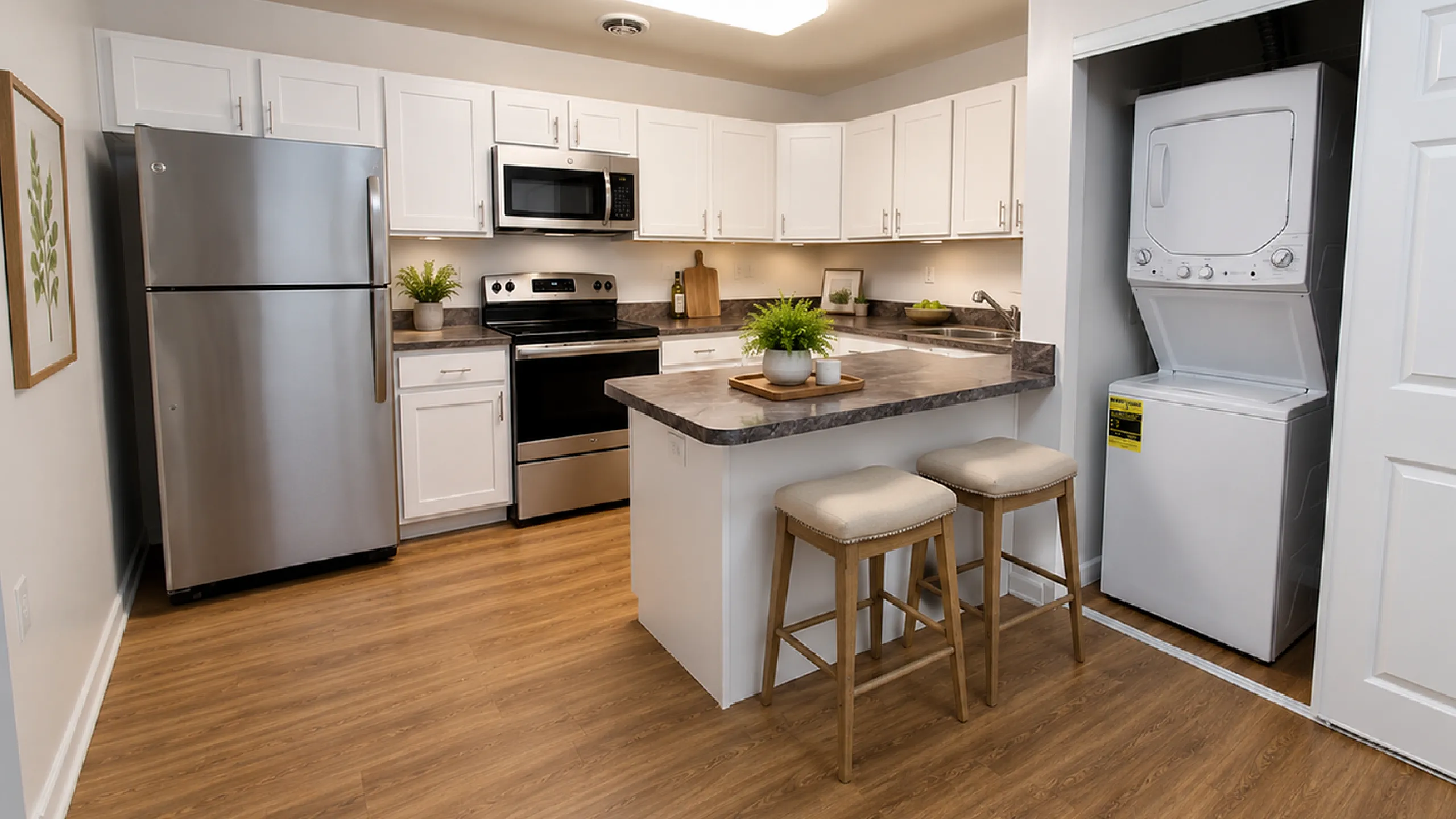 Contemporary kitchen with sleek stainless steel appliances, elegant white cabinetry, and convenient in-unit washer-dryer. Cozy breakfast bar seating with stylish wood flooring.