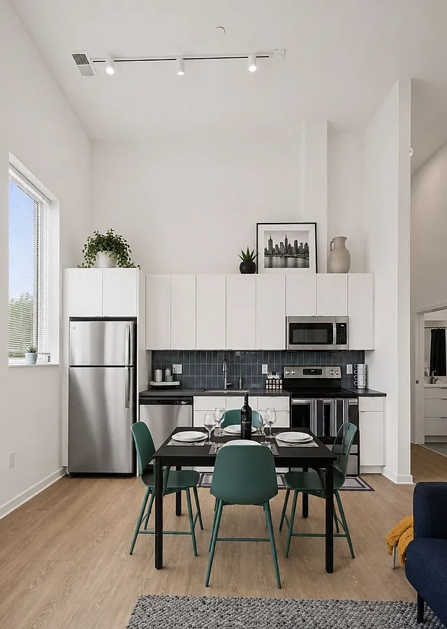 Modern kitchen with sleek white cabinetry, stainless steel appliances, and a cozy dining area with green chairs, perfect for elegant dining.