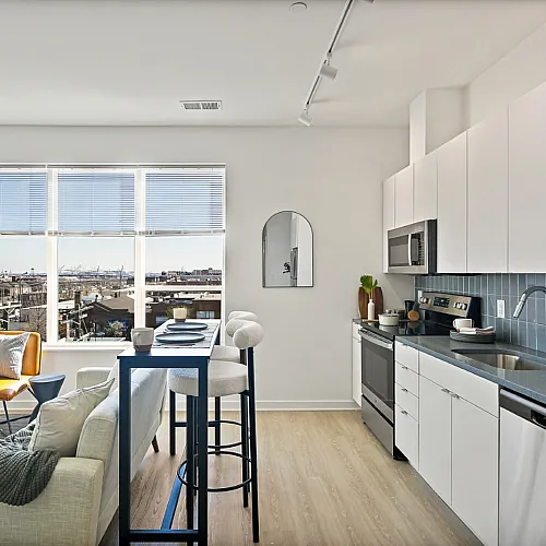 Bright and modern open-plan kitchen and living area with stylish furnishings, large window with city views, and sleek stainless steel appliances creating an inviting atmosphere.