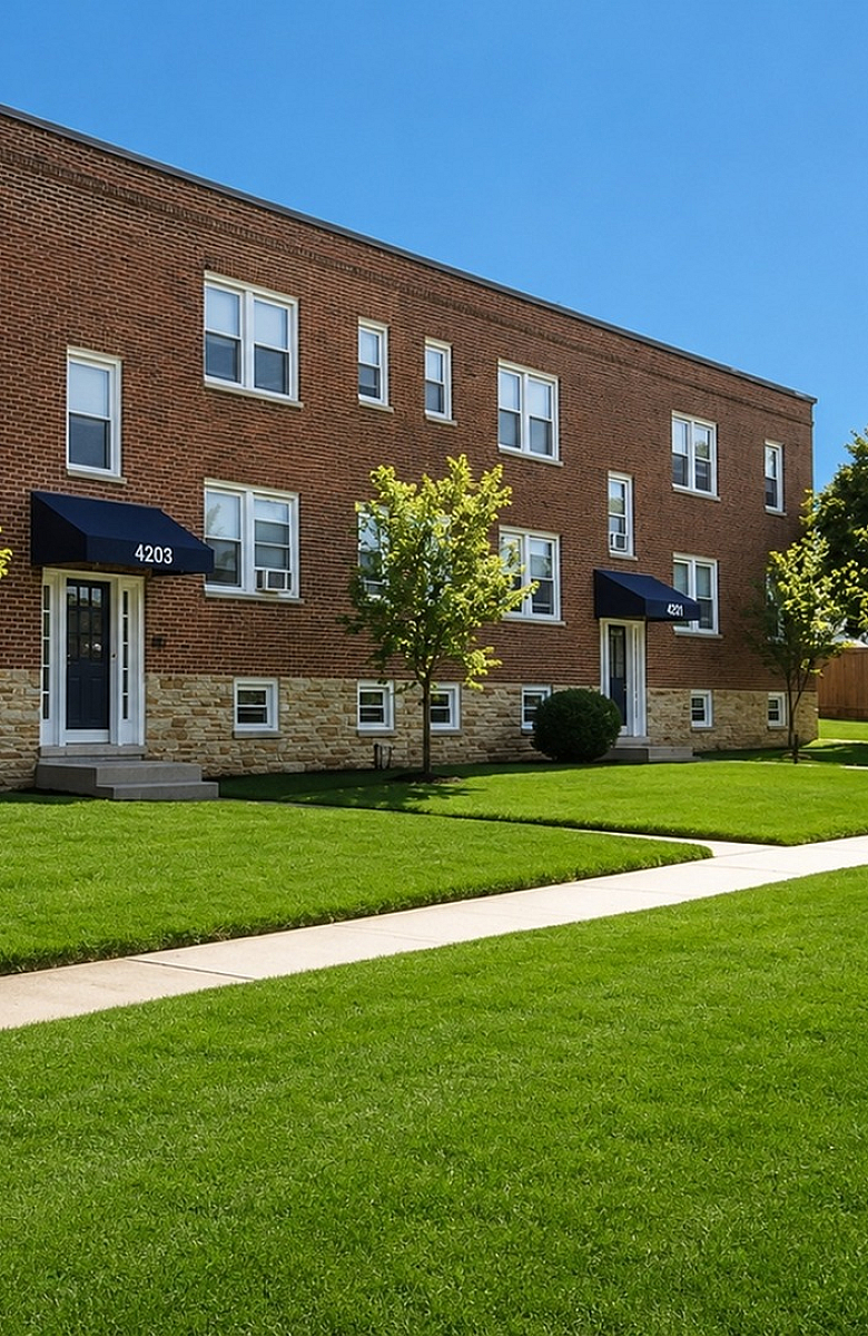 Charming brick apartment building with lush green lawns and manicured pathways, offering a welcoming and serene environment.