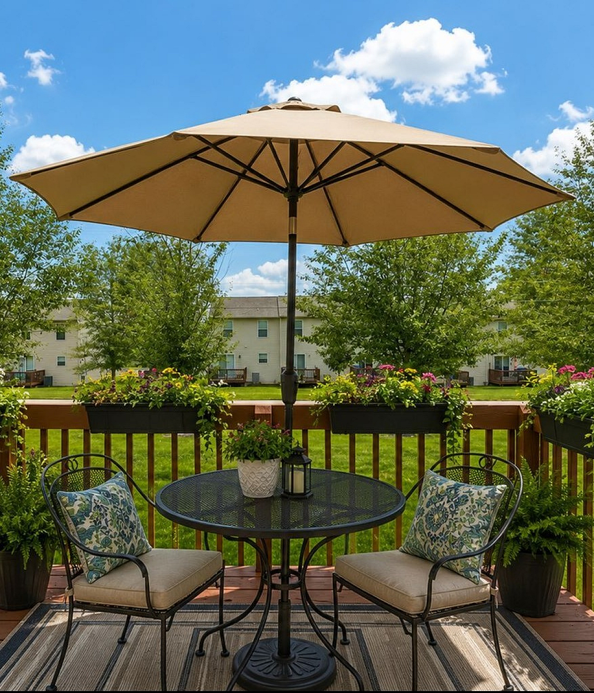 Charming outdoor patio with elegant metal table set, surrounded by lush greenery and colorful flowers, perfect for relaxing under a large umbrella.