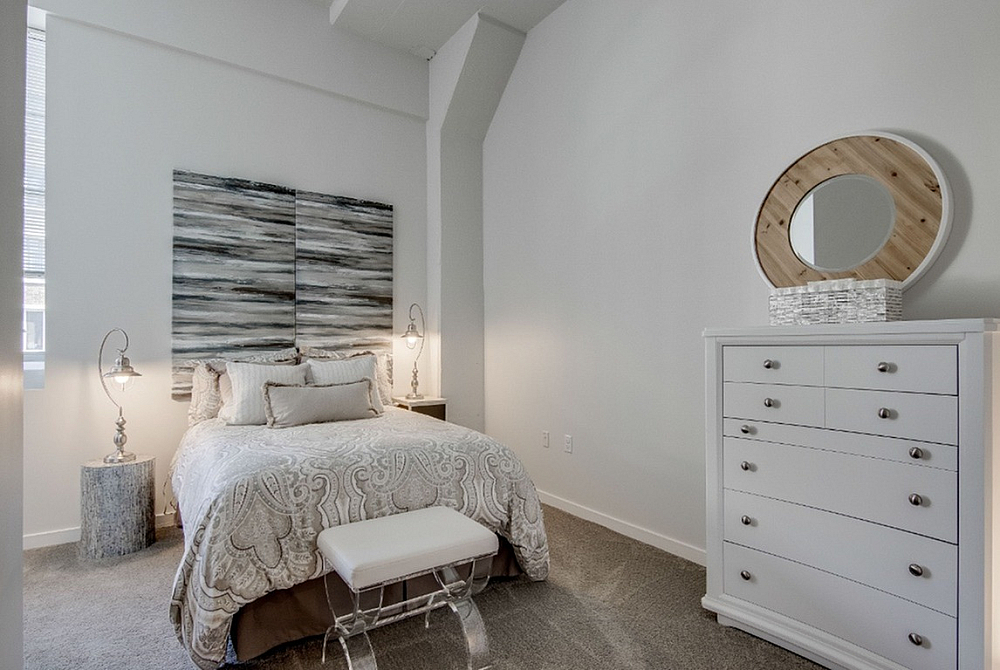 Elegant bedroom with cozy bed, chic bedside lamps, stylish abstract art, and a modern white dresser with a unique circular mirror accent.