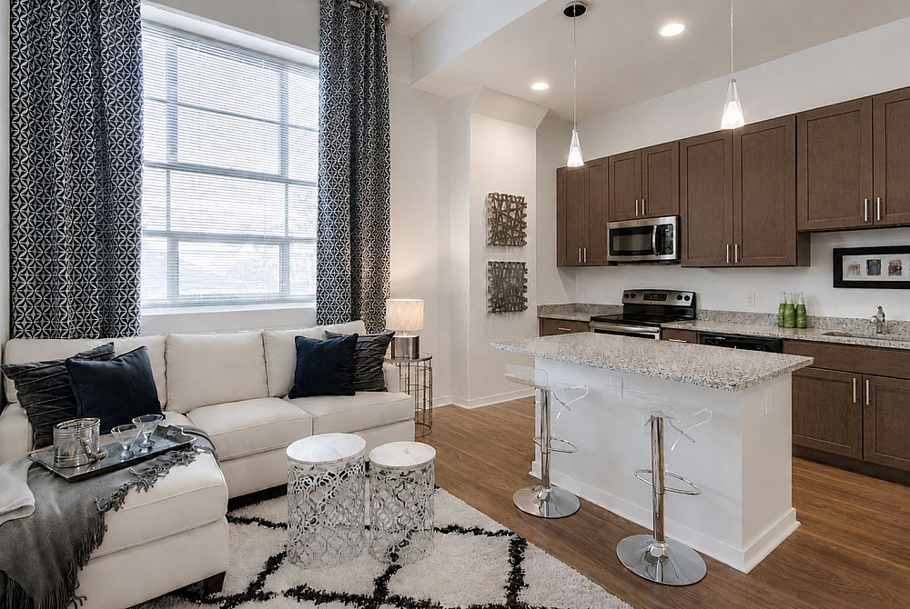 Modern apartment with elegant living area featuring a plush white sofa, chic decor, and bright kitchen with granite countertops and dark wood cabinets.
