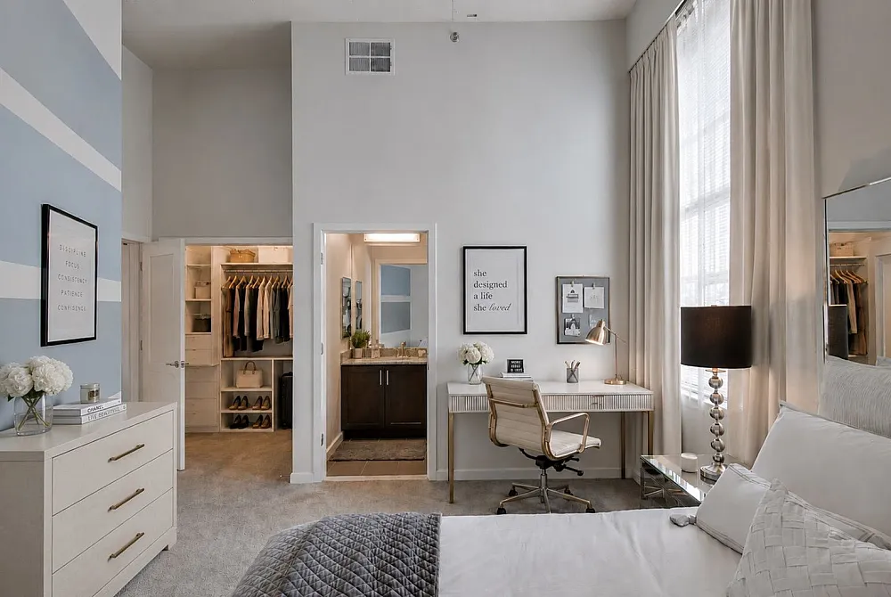 Elegant bedroom with stylish decor featuring a spacious walk-in closet, a cozy work area, and abundant natural light through large windows.