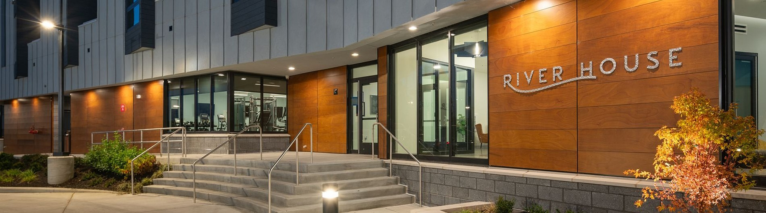 Modern apartment entrance at River House with sleek architectural design, warm wooden accents, and inviting evening lighting.