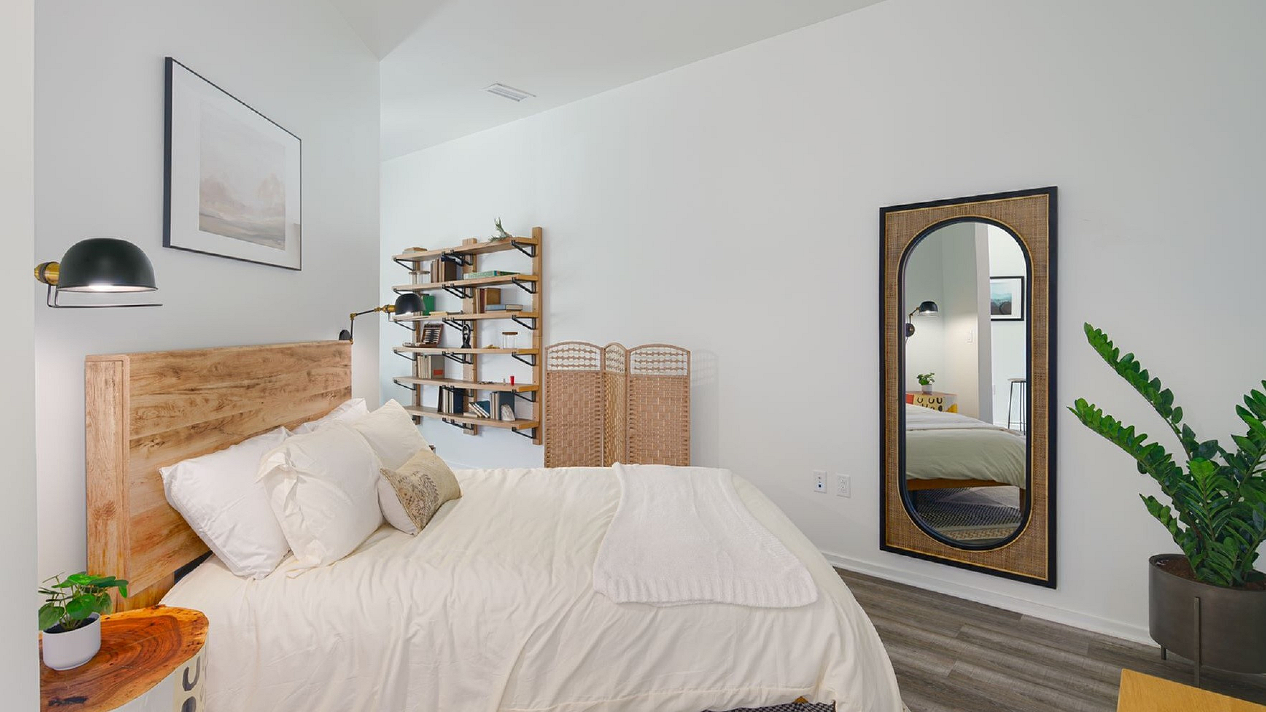 Inviting bedroom with elegant wooden headboard, modern wall lamps, stylish bookshelf, and a full-length mirror, creating a serene retreat.