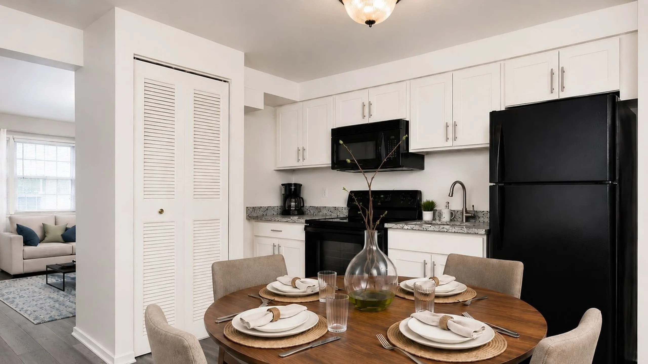 Modern open kitchen and dining area with elegant wooden table set, stylish black appliances, and cozy living room visible in the background.