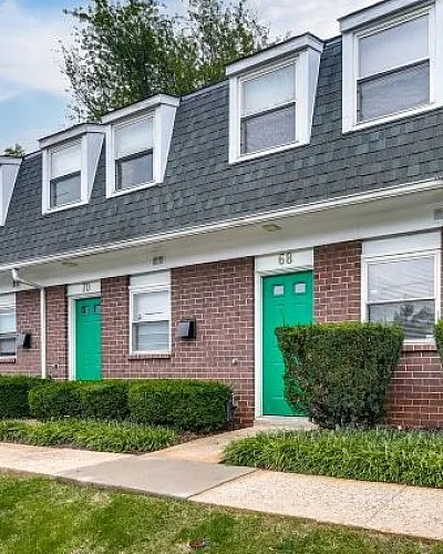 Charming townhouse facade with colorful doors, lush greenery, and modern dormer windows.