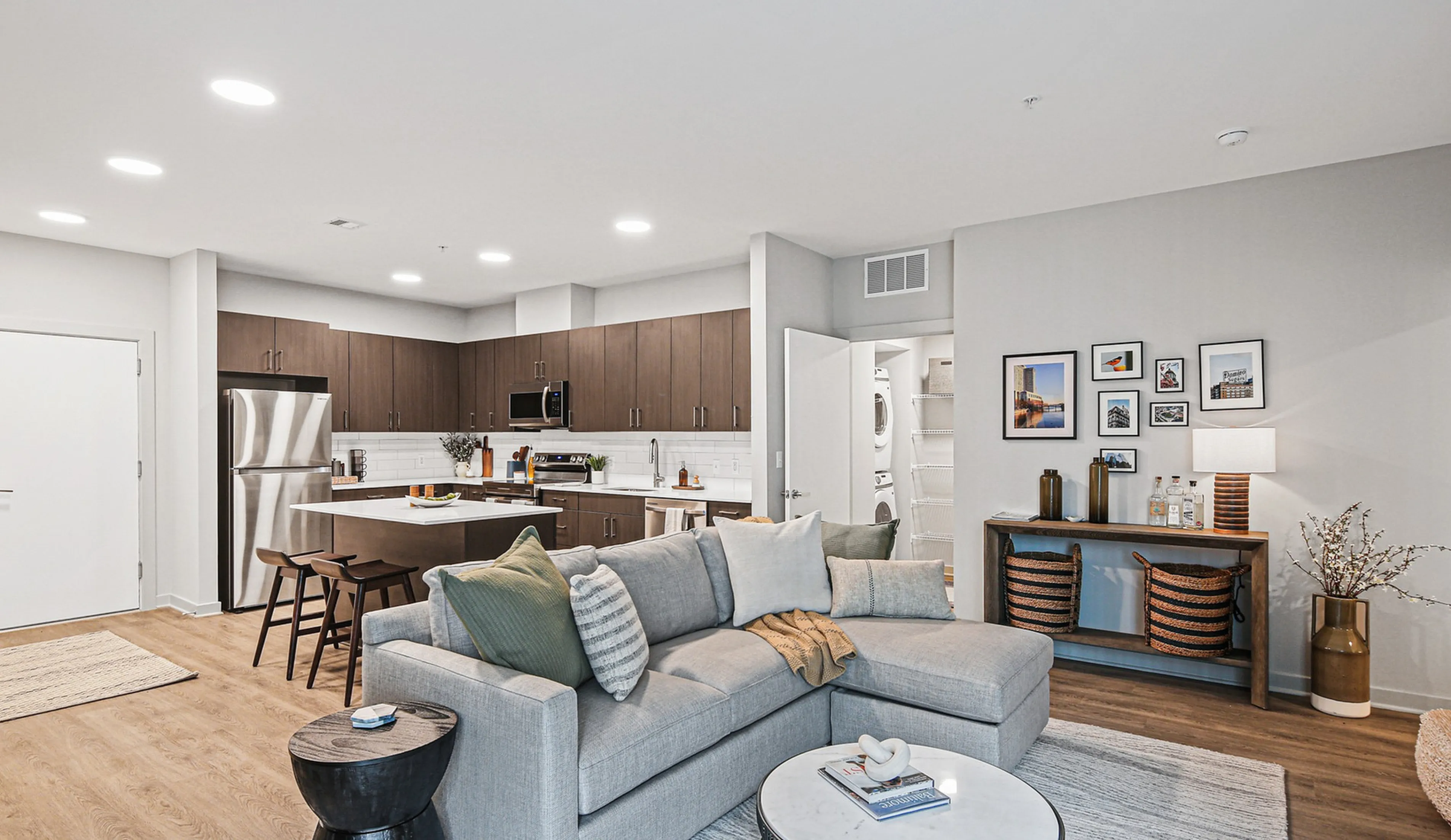 Contemporary open-concept living area with modern kitchen, cozy grey sofa, stylish decor, and abundant natural light.
