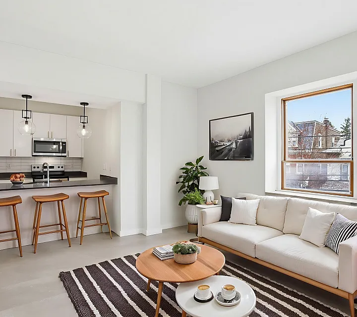 Chic and modern living space featuring a cozy sofa, stylish kitchen with barstools, and large windows offering natural light.
