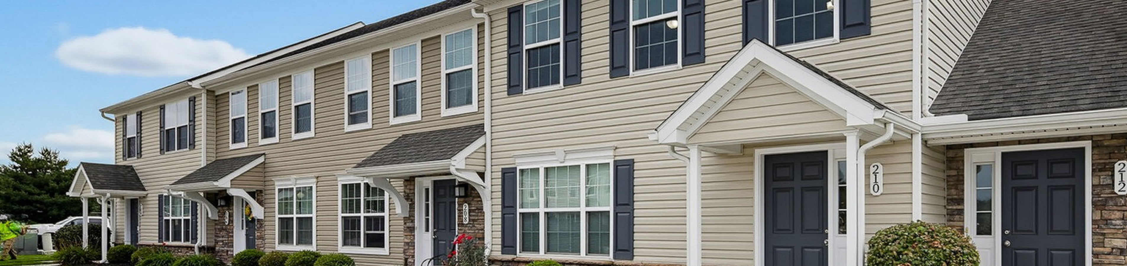 Charming townhouse exterior with modern design, pristine landscaping, and inviting entries under a bright blue sky.