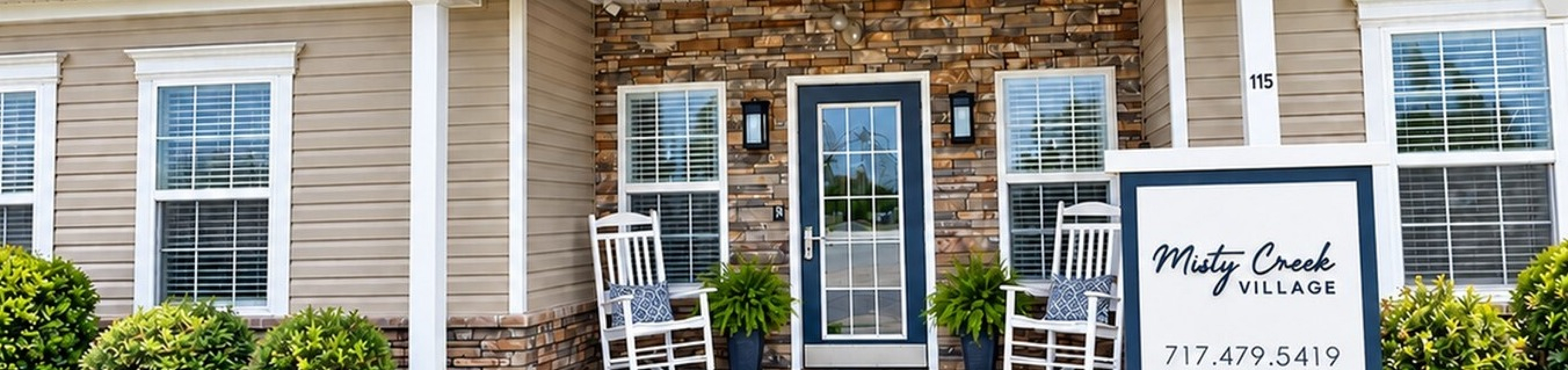 Charming single-story clubhouse of Misty Creek Village with inviting rocking chairs on a sunny day, surrounded by lush greenery.