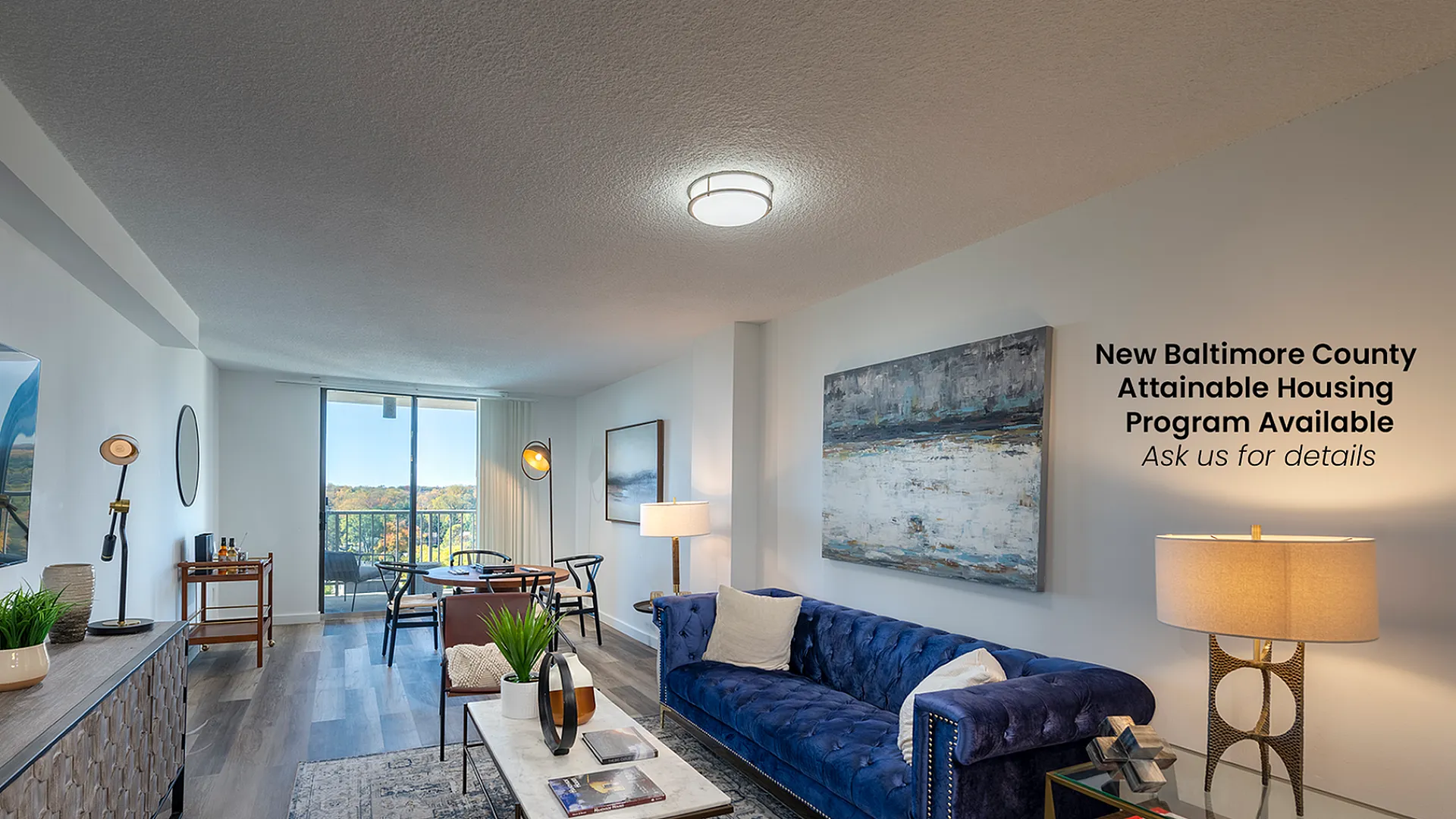 Modern living room in Baltimore County apartment, featuring a plush blue sofa, elegant decor, and a balcony view of scenic landscapes.