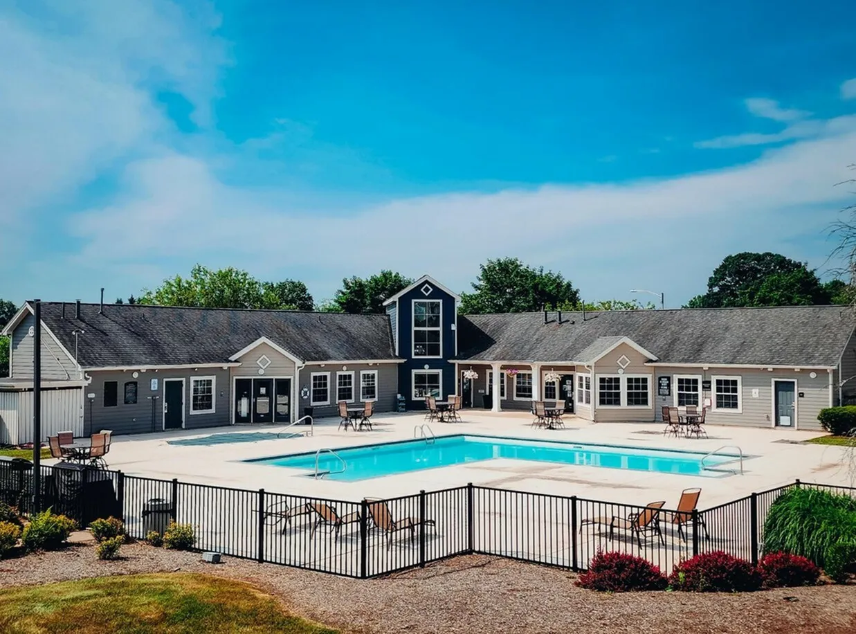 Charming residential complex showcasing a sparkling outdoor pool surrounded by a modern clubhouse and lush greenery under a clear blue sky.