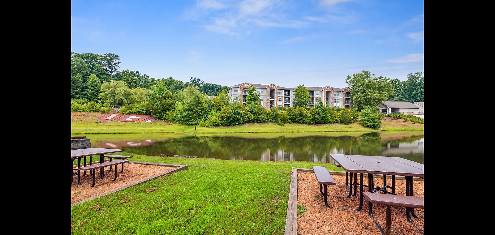 Charming apartment complex with stunning lakeside views, surrounded by lush greenery and featuring convenient outdoor picnic tables.