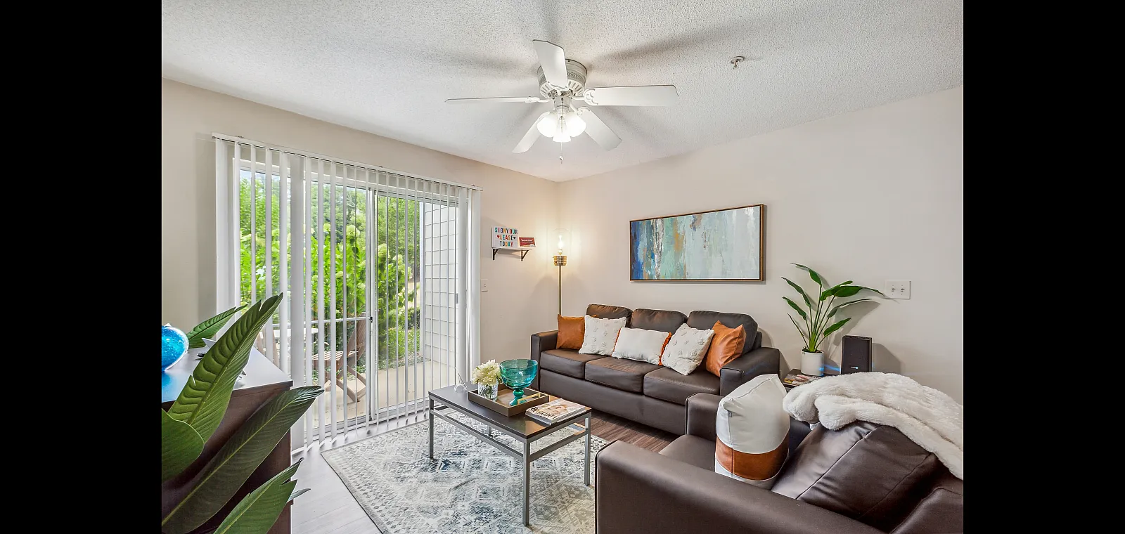 Bright and cozy living room with modern decor, featuring comfortable leather sofas, a stylish coffee table, and a large window with lush garden views.