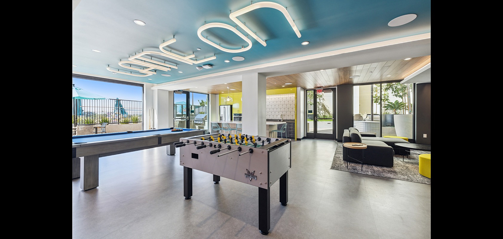 Vibrant and modern community lounge featuring a foosball table, pool table, cozy seating area, and bright open spaces with natural light.