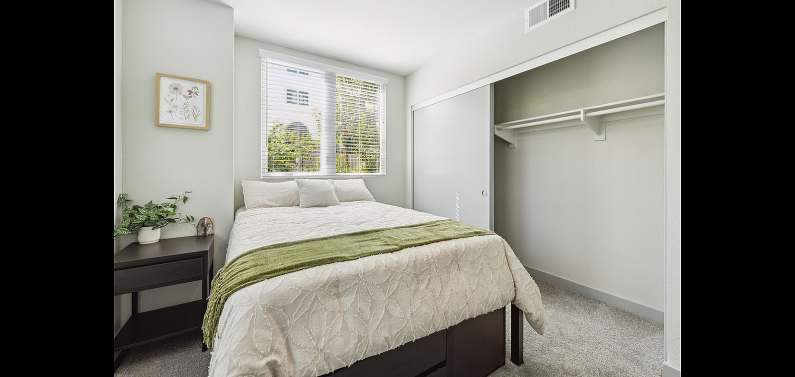 Bright and airy bedroom featuring a cozy bed with elegant bedding, large window allowing natural light, and a spacious built-in closet.