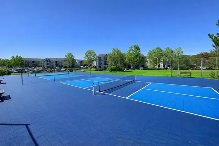 Vibrant outdoor tennis courts with a backdrop of lush greenery and modern apartment buildings, ideal for sporty living and relaxation.
