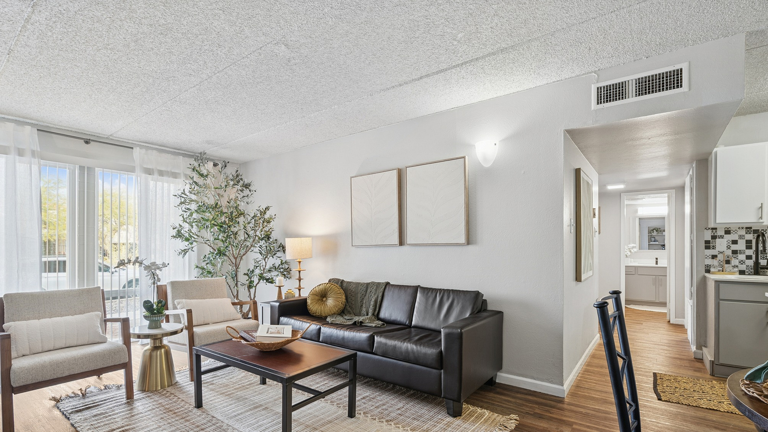 Chic apartment living room with sleek leather couch, modern chairs, and abundant natural light, complemented by tasteful decor and elegant hardwood floors.
