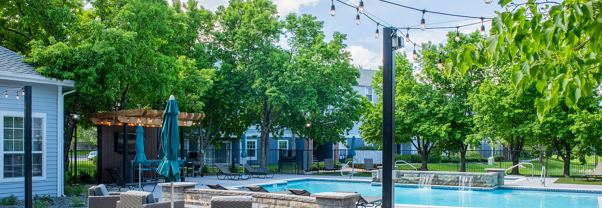 Charming outdoor space featuring a sparkling pool, cozy seating with fire pit, and lush greenery under string lights.