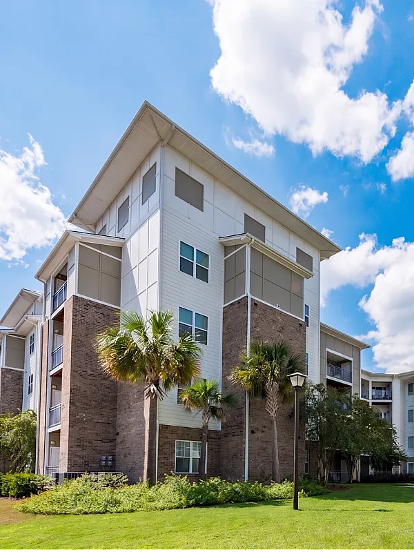 Modern apartment complex with beautiful landscaping, palm trees, and expansive blue skies.