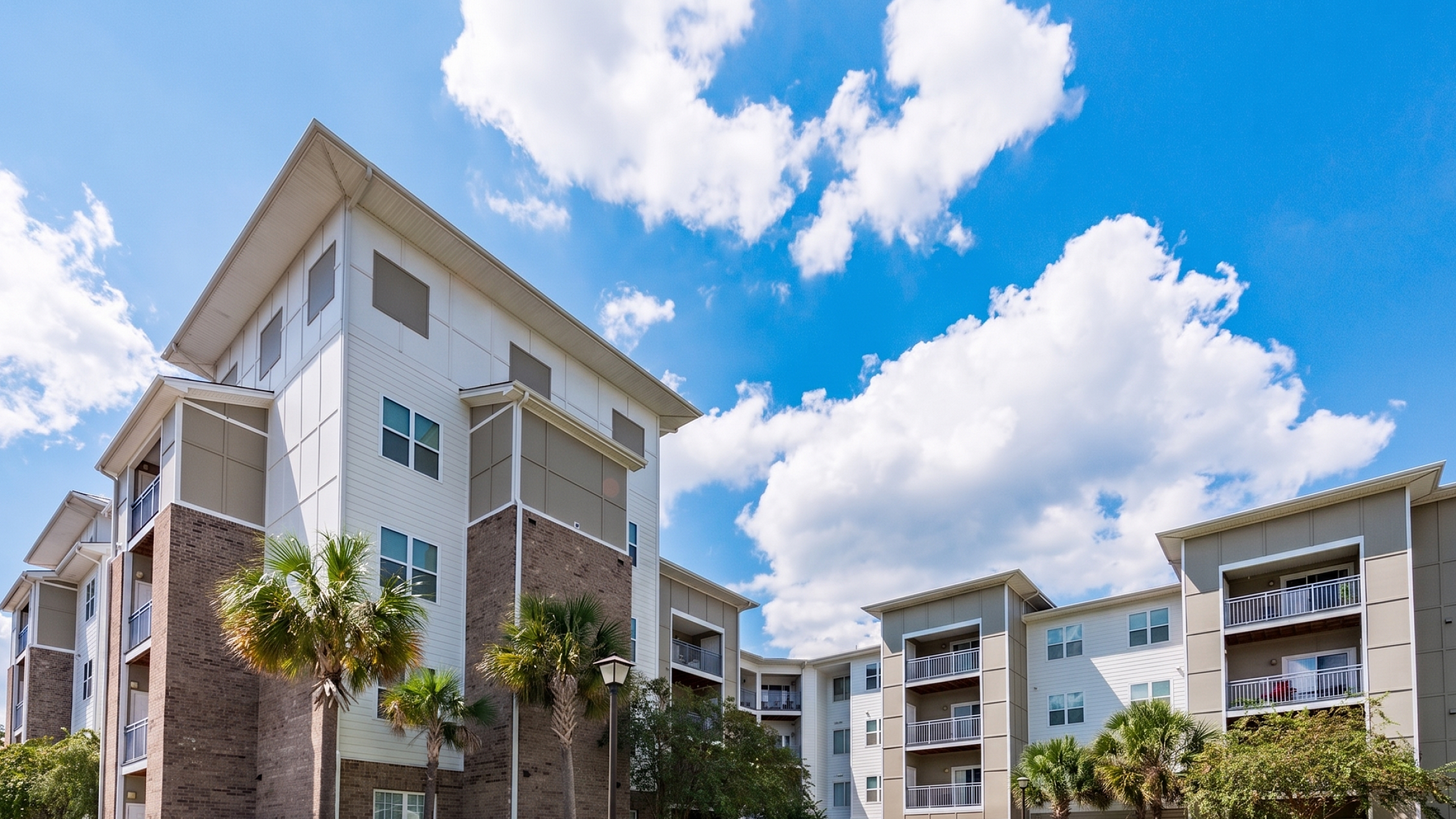 Modern apartment complex with spacious balconies, lush landscaping, and a clear blue sky backdrop.
