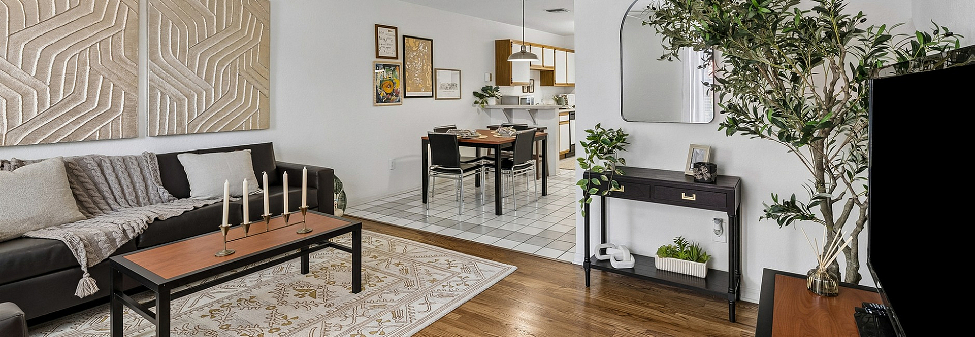 Inviting living room with elegant decor, featuring a comfortable sofa, chic wall art, and a stylish wooden coffee table. The open-plan design leads to a cozy dining area and modern kitchen, creating a seamless flow.