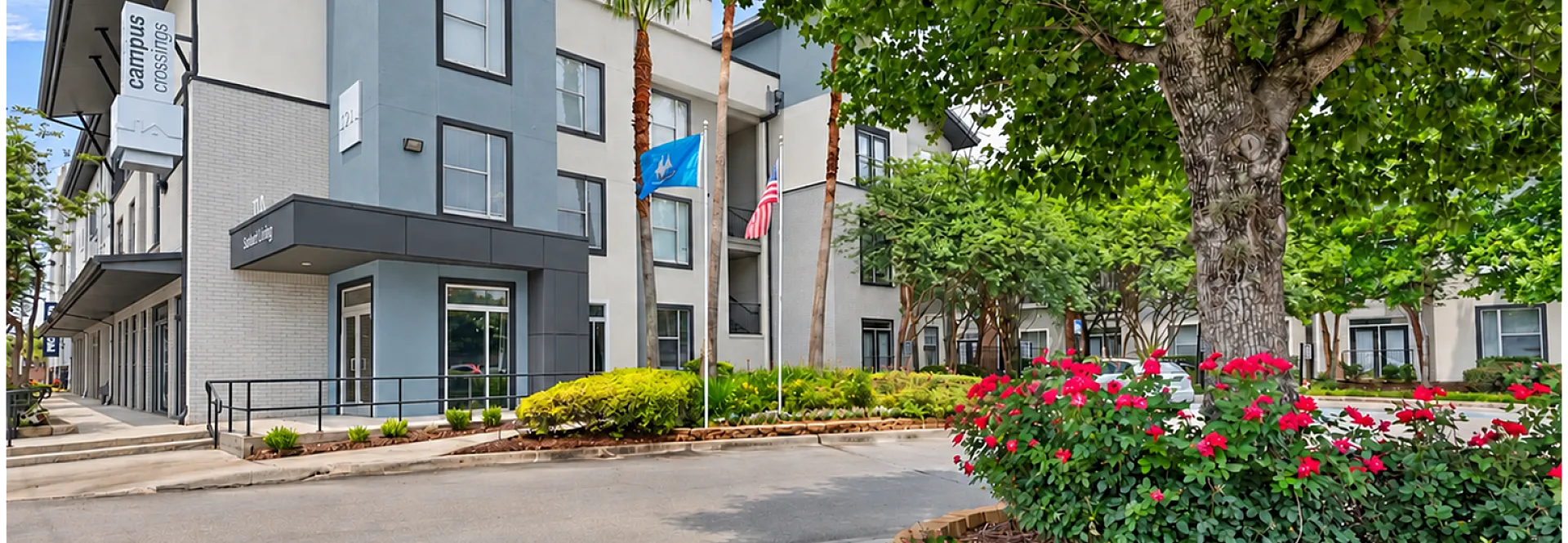 Modern apartment building with sleek design, surrounded by lush landscaping and vibrant flowers, offering a welcoming entrance and spacious greenery.