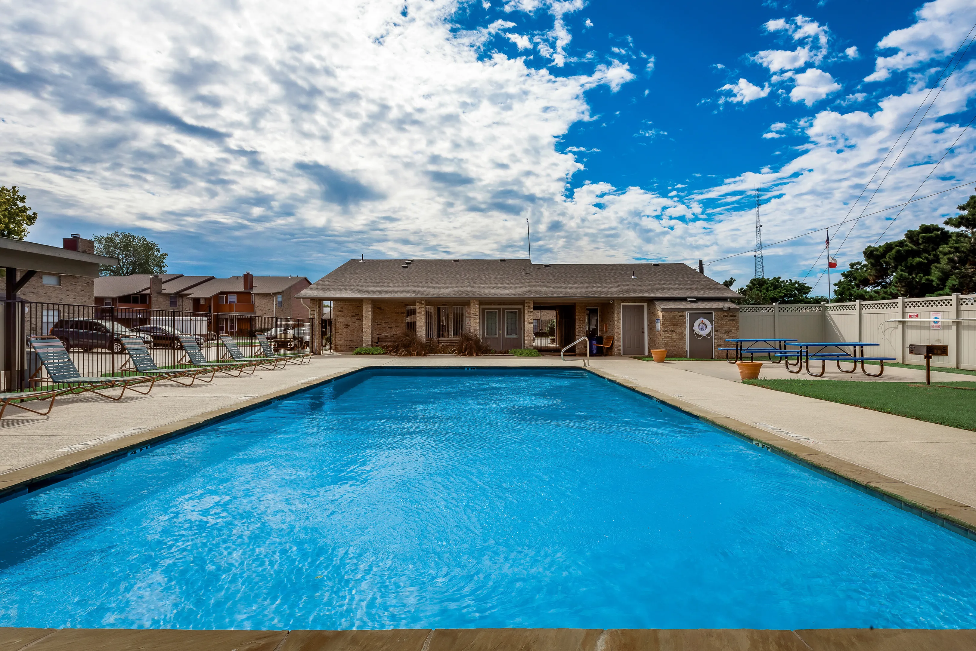 Inviting swimming pool at a stylish residential complex, featuring lounge chairs, a sunny patio, and modern amenities under a clear blue sky.