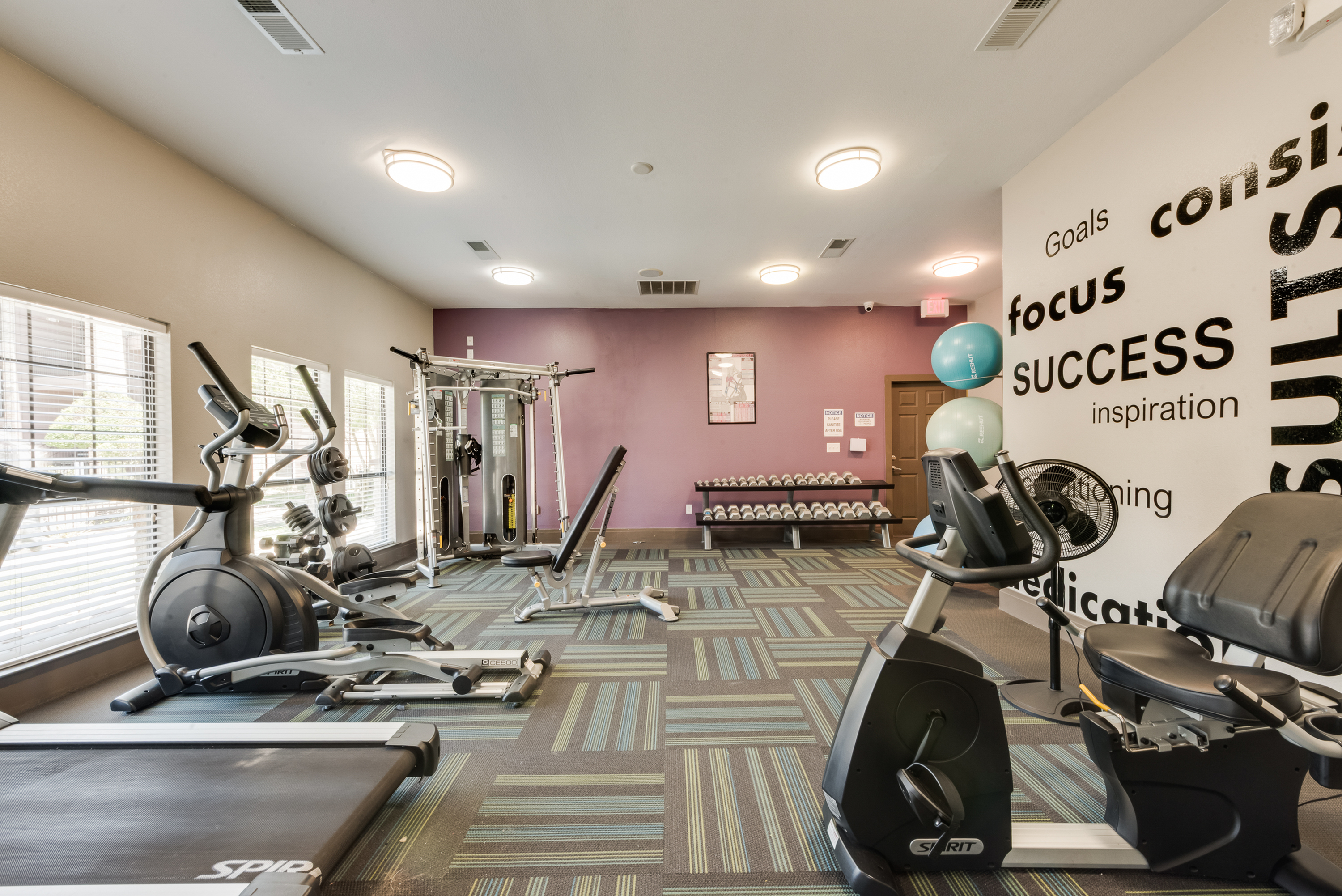 Modern fitness center with state-of-the-art gym equipment, motivational wall decor, and ample natural lighting.