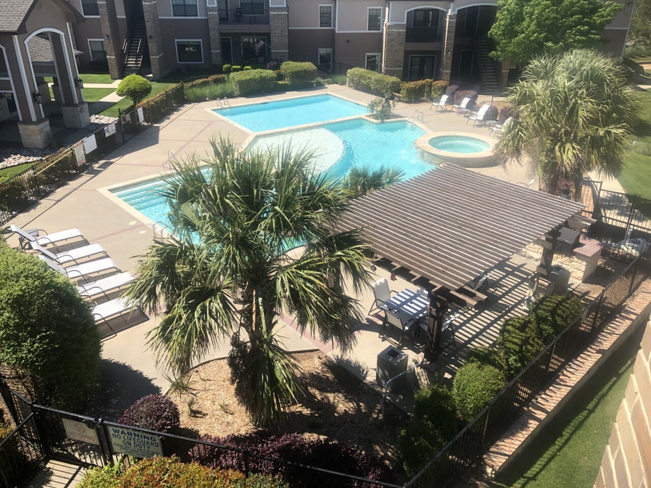 Inviting apartment complex pool area with lush greenery, comfortable lounge chairs, and a stylish pergola for shaded relaxation.