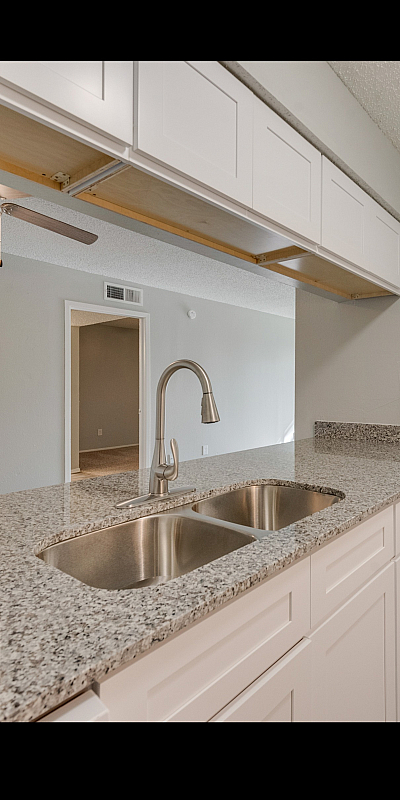 Modern kitchen with sleek granite countertops, dual sink, and elegant cabinetry leading into a bright living area with ceiling fan.