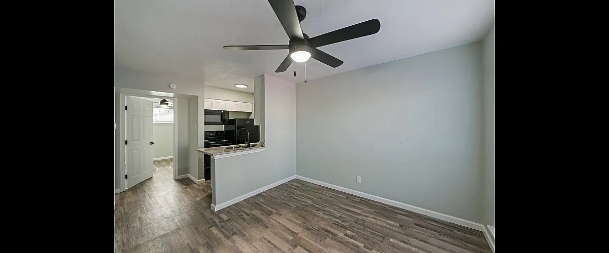 Modern apartment interior with sleek kitchen, stylish ceiling fan, and elegant wood flooring.