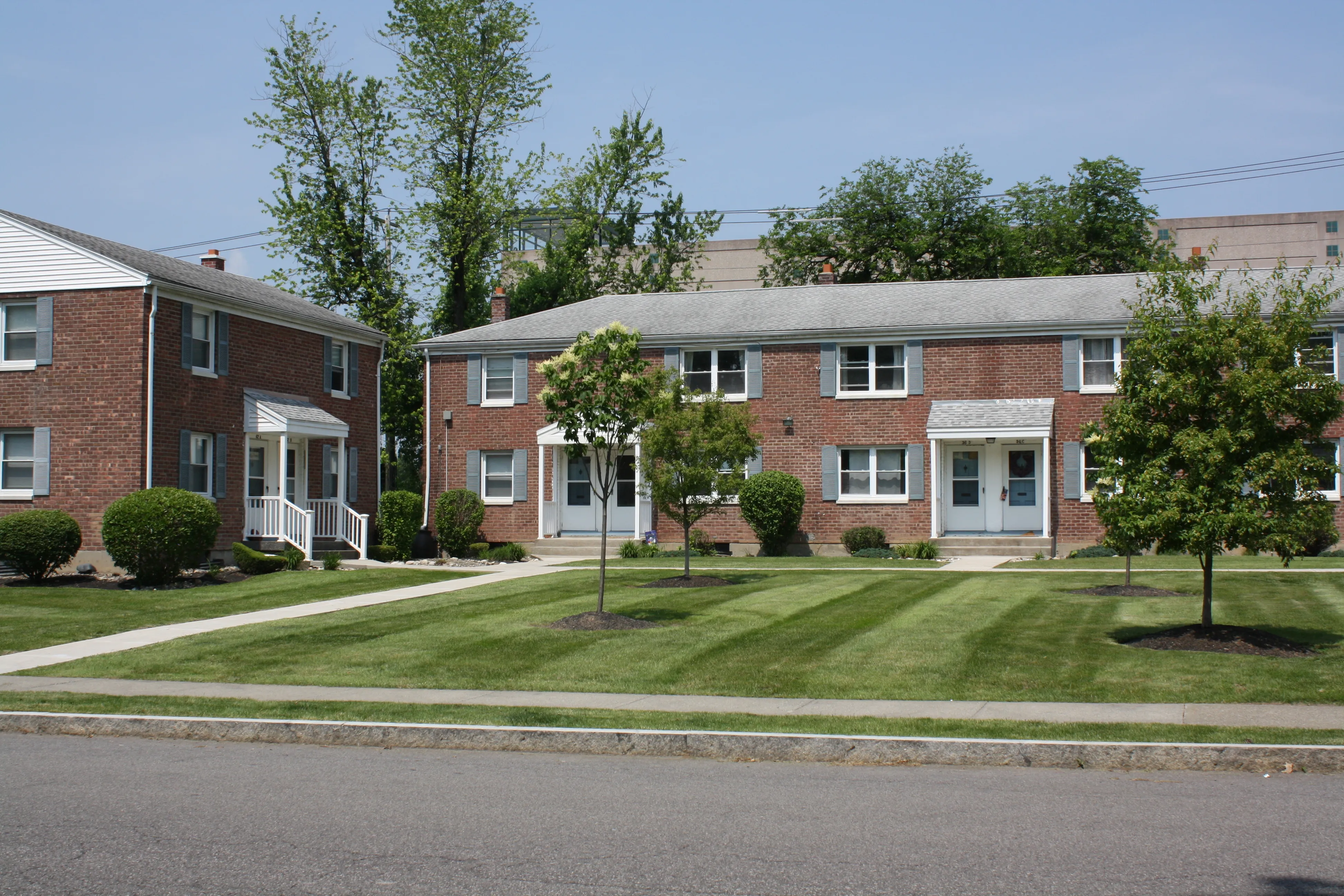 Inviting suburban apartment complex featuring charming red brick buildings, lush green lawns, and mature trees.