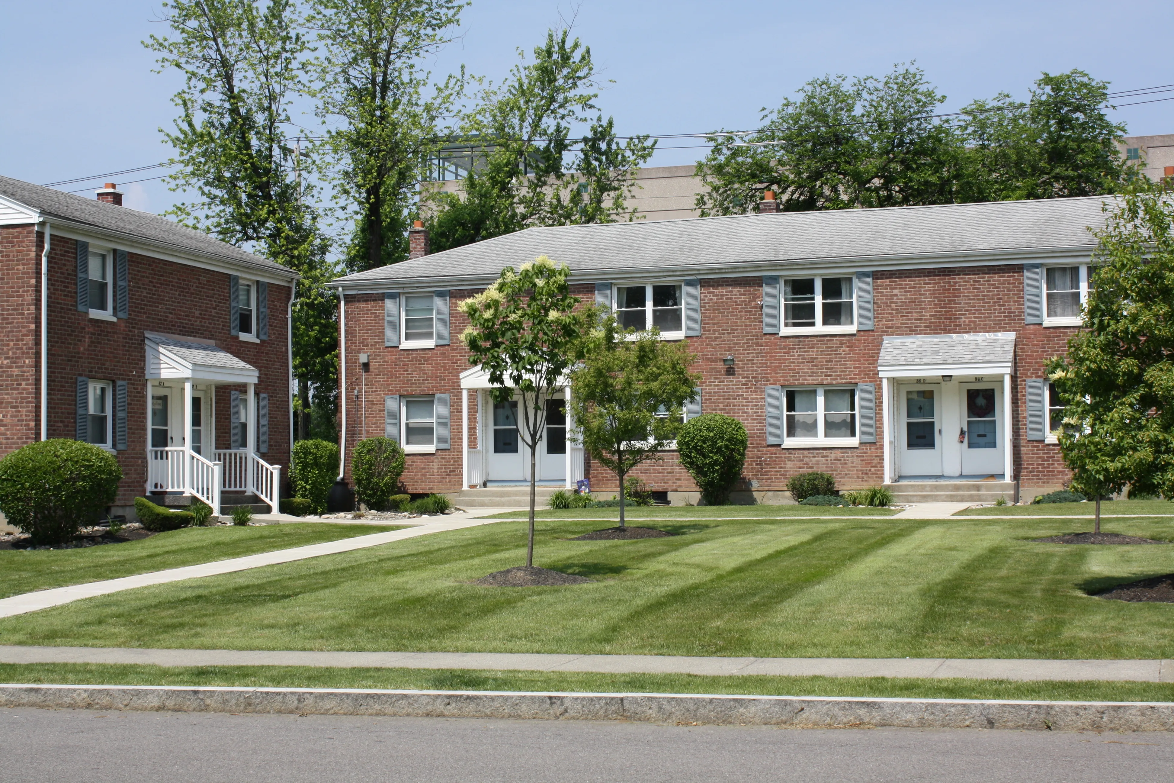 Charming brick townhouses with manicured lawns and inviting front porches, perfect for a cozy suburban lifestyle.