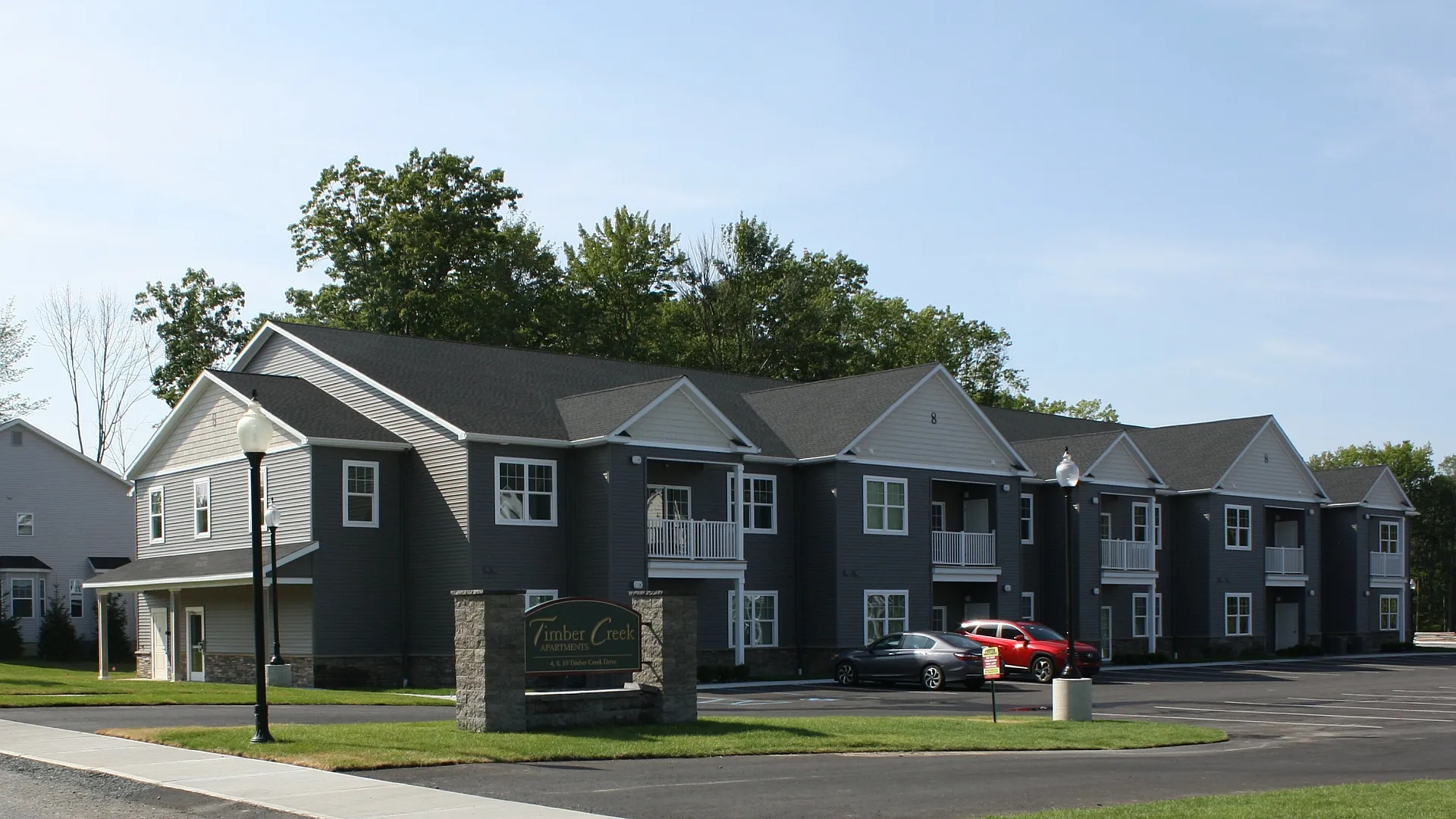 Modern Timber Creek Apartments with elegant gray exterior, roomy balconies, and well-manicured landscaping, set against a tranquil wooded backdrop.