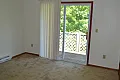 Bright and cozy bedroom with plush carpet and sliding glass doors opening to a serene balcony with lush green views.