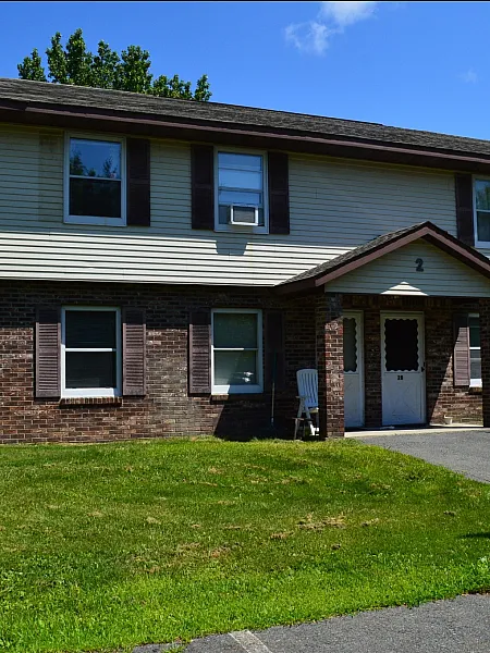 Charming two-story townhouse with classic brick facade and lush green lawn, featuring convenient reserved parking.